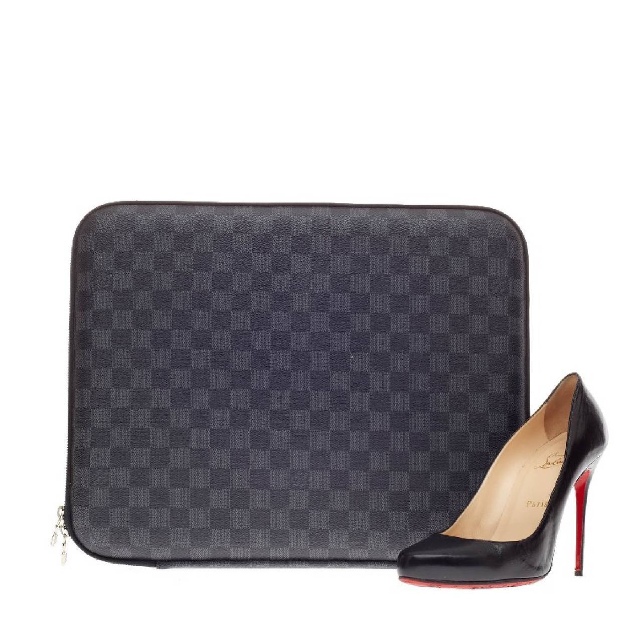 This authentic Louis Vuitton Laptop Sleeve Damier Graphite Canvas 15 designed from iconic damier graphite canvas is a slim laptop case that features silver hardware accents and a zip-around closure. The case's black foam interior showcases an