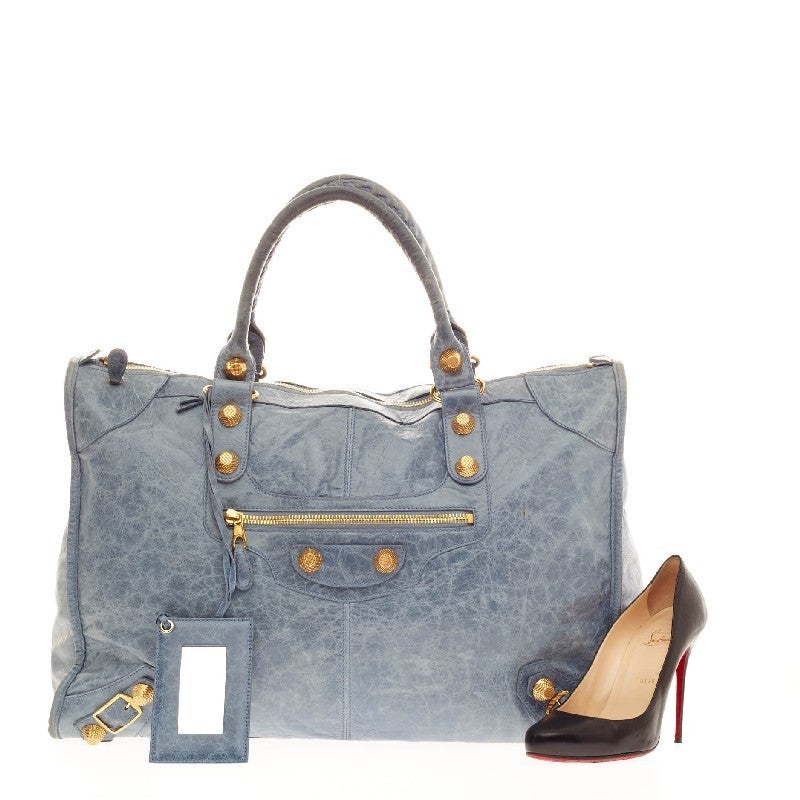 This stunning authentic Balenciaga Weekender Giant Studs Leather is an instant luxurious classic. This desirable bag, constructed from distressed sky blue leather, features braided woven handle straps, giant gold-tone hardware and zipper pocket on