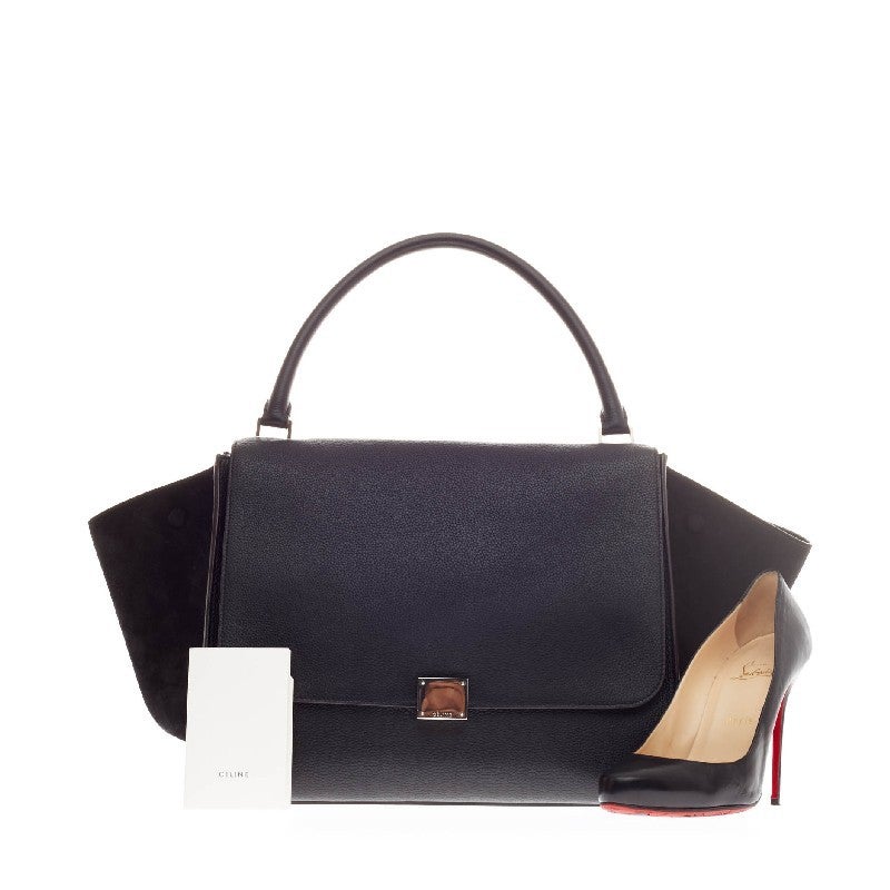This authentic Celine Trapeze Suede Large with a minimalist design is a fashionista's dream. Constructed in sleek black leather with matching suede wings, this oversized tote is accented with silver hardware and a full frontal flap with a square