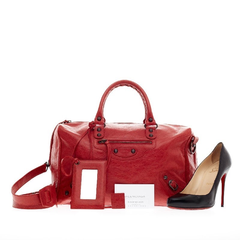This authentic Balenciaga Polly Classic Studs Leather is the perfect daily bag for on-the-go fashionista. Crafted from poppy red distressed leather, this functional duffle bag features dual braided top handles, front zipped pocket and a removable
