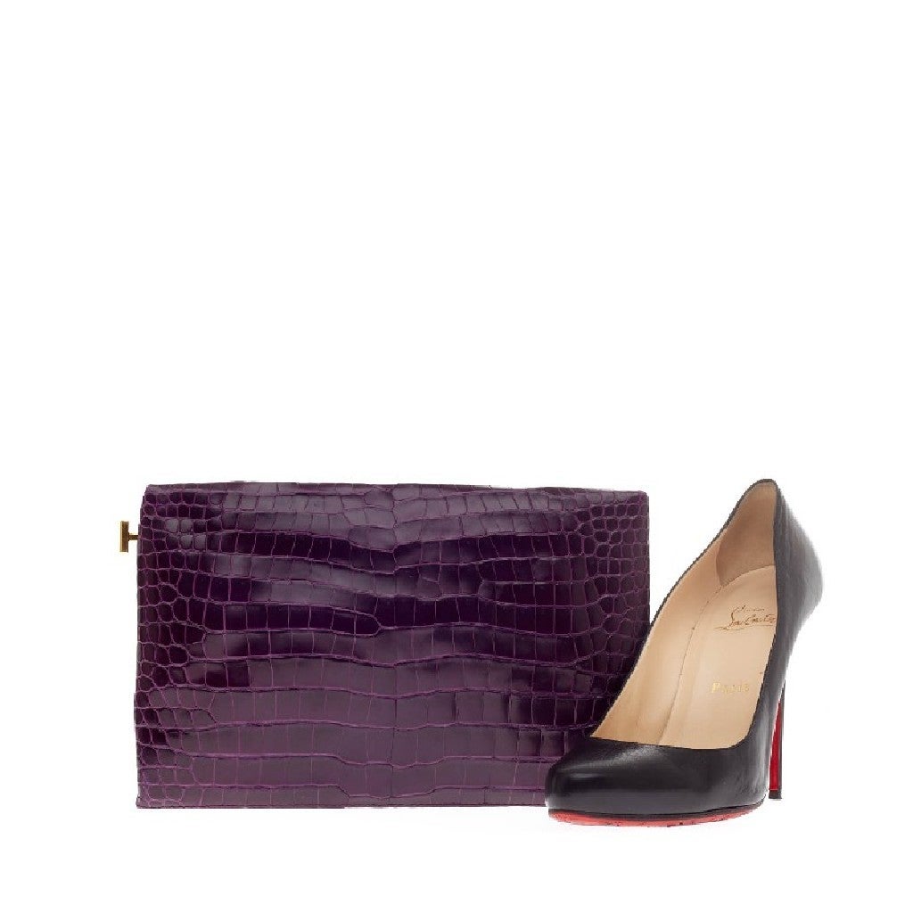 This authentic Tom Ford Frame Clutch Crocodile showcases the designer's luxurious style with a minimalist flair. Crafted in genuine royal purple crocodile skin, this small, sleek frame clutch features a simple silhouette and polished gold top frame