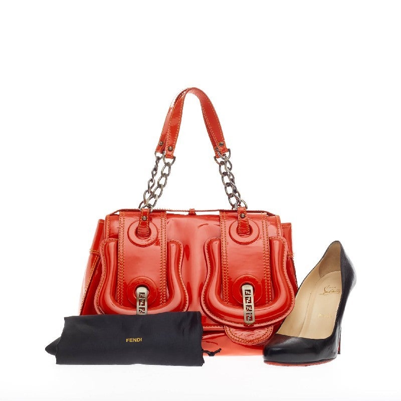 This authentic Fendi B. Bag Patent Medium is a chic bag with a roomy construction that is ideal for work and everyday use. Crafted from red orange patent leather, this bag features oversized buckle details with brass logo hardware, snap lock