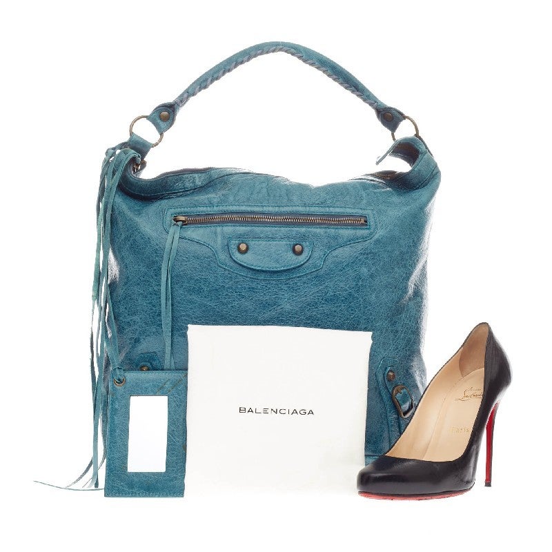 This authentic Balenciaga Day Hobo Classic Studs Leather is a go-to accessory that fits everyday essentials. Crafted in muted turquoise leather, this spacious hobo is accented with an intertwined braided leather top handle, long fringes on front