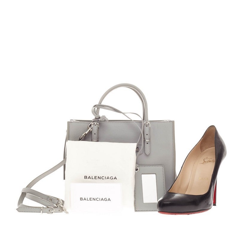 This authentic Balenciaga Papier A4 Zip Around Classic Studs Leather Mini is a modern-minimalistic accessory that can add glam to a casual wardrobe. Crafted in light grey leather, this petite, boxy tote features dual-rolled slim handles, zippered