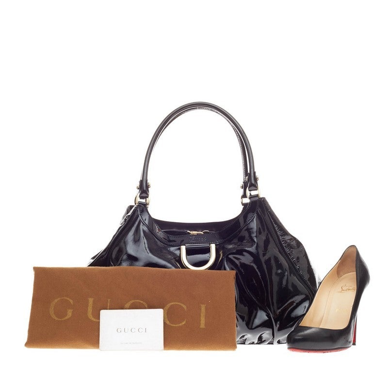 This authentic Gucci D Gold Shoulder Bag Patent Large is perfect for everyday use. Crafted in sleek black patent leather, this bag features tall dual-rolled handles, base studs, gold-tone hardware accents, embossed Gucci script logo and signature D