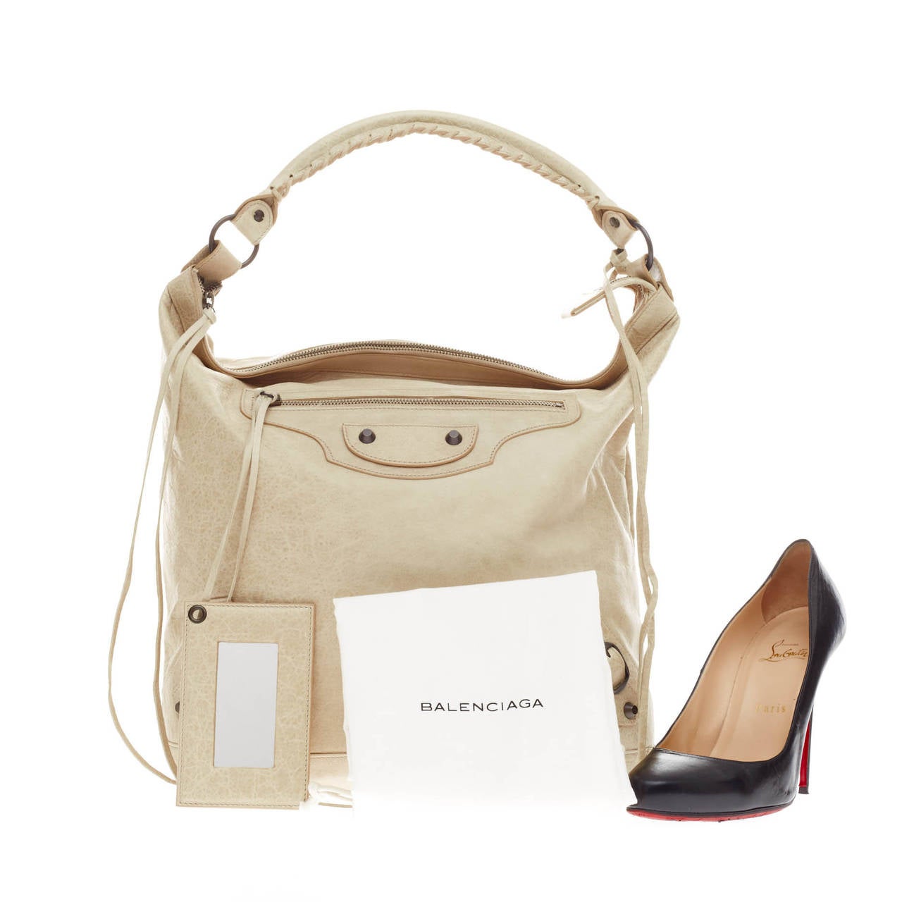 This authentic  Balenciaga Day Hobo Classic Studs Leather is a go-to essential that fits everyday essentials. Crafted in ivory off-white leather, this spacious hobo is accented with an intertwined braided leather top handle, long fringes on front