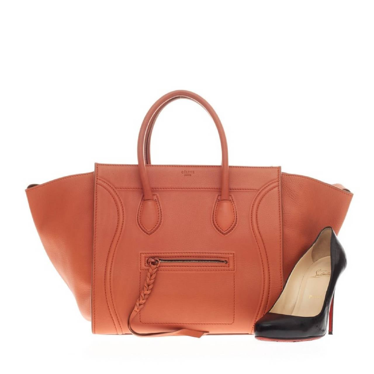 This authentic Celine Phantom Smooth Leather Medium is one of the most sought-after bags beloved by fashionistas. Crafted from vivid burnt orange smooth leather, this oversized minimalist tote features a braided zipper pull, dual-rolled handles, zip
