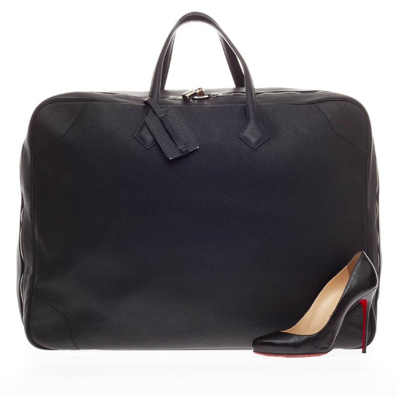 This authentic Hermes Victoria II Travel Clemence 50 boasts of a large stature perfect for luxurious traveling. Created in supple black clemence leather, this oversized travel bag features side leather tabs, palladium hardware accents, tall