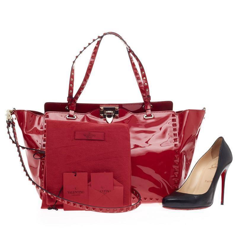 This authentic Valentino Rockstud Tote Patent Medium presents a sleek design with an edgy twist made for daring fashionistas. Crafted from striking red patent leather, this popular tote features signature matte-red pyramid stud border and strap