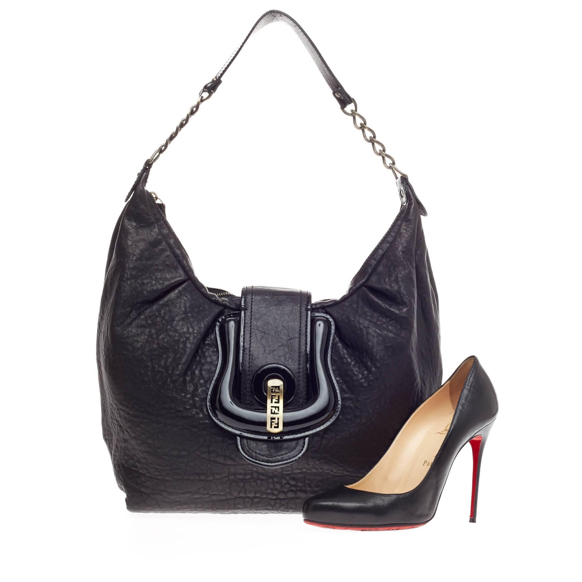 This authentic Fendi B. Hobo Leather is ideal for everyday use. Crafted in black textured pebbled leather and patent detailing, this hobo features chain straps with leather pads, giant flap belt and buckle details, and gold-tone hardware accents.