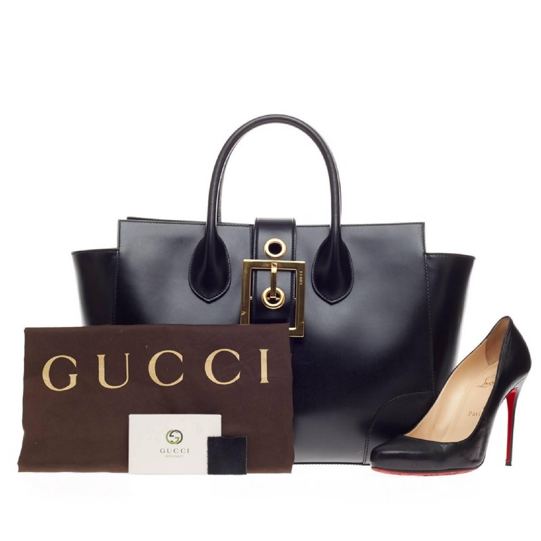 This authentic Gucci Lady Buckle Top Handle Leather is sleek and functional made for your everyday look. Crafted in smooth black calfskin leather, this structured tote features an oversized top flap buckle belt detail with engraved Gucci logo,