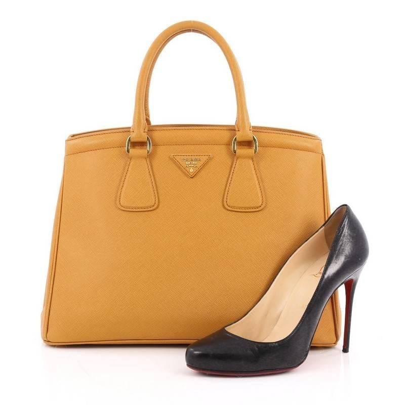 This authentic Prada Parabole Handbag Saffiano Leather Medium is elegant in its simplicity and structure. Constructed in dark yellow saffiano leather, this sleek tote features dual-rolled leather handles, raised Prada logo, protective base studs,