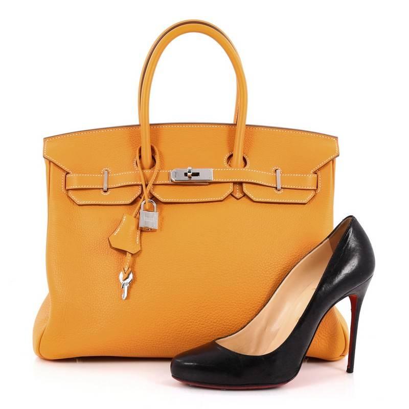 This authentic Hermes Birkin Handbag Moutarde Clemence with Palladium Hardware 35 showcases subtle elegance. Finely crafted in beautiful, Moutarde orange yellow clemence leather, this piece features dual-rolled top handles, frontal flap, turn-lock