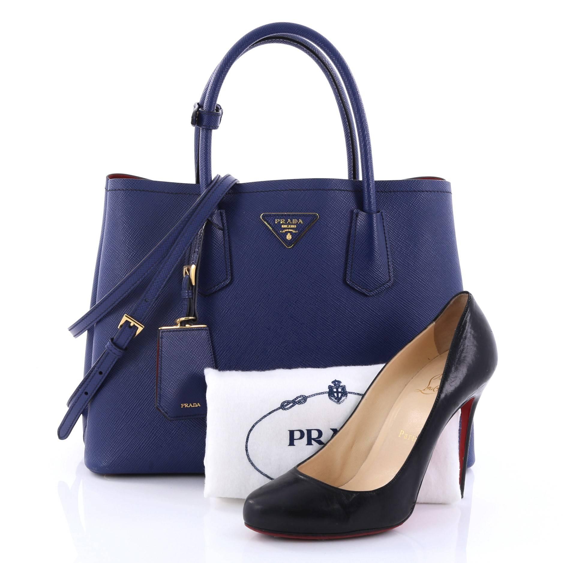 This authentic Prada Cuir Double Tote Saffiano Leather Medium is elegant in its simplicity and structure. Crafted from sturdy blue saffiano leather, this tote features dual-rolled handles, side snap buttons, Prada's trademark triangle logo at the