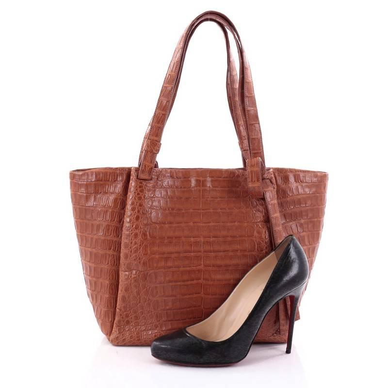 This authentic Nancy Gonzalez Tote Crocodile Medium showcases a perfect polished look made for daily or work excursions. Crafted from genuine orange crocodile skin, this simple yet elegant tote features dual tall handles, protective base feet, a