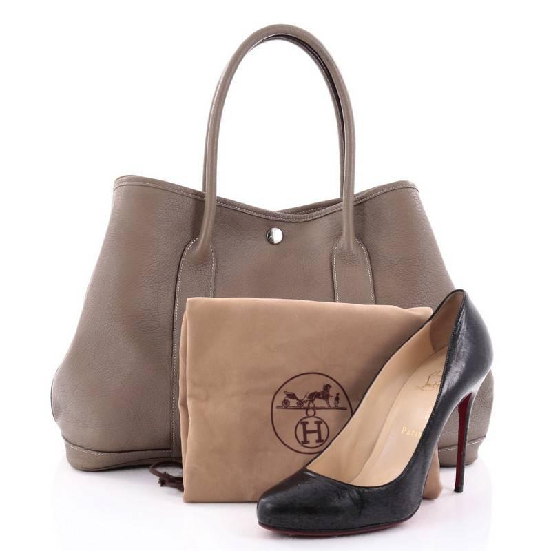 This authentic Hermes Garden Party Tote Leather 36 is an elegant and simple tote made for all seasons. Crafted from etoupe leather, this chic everyday tote features dual-rolled leather top handles, stand-out contrast stitching, palladium button