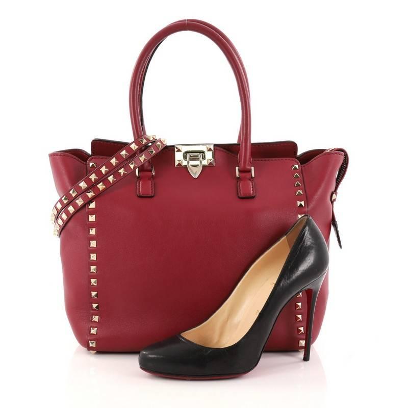 This authentic Valentino Rockstud Tote Rigid Leather Medium is a stylish and iconic bag that is one of today's most sought-after styles. Crafted from beautiful redk rigid leather, this chic tote features signature gold pyramid stud border,