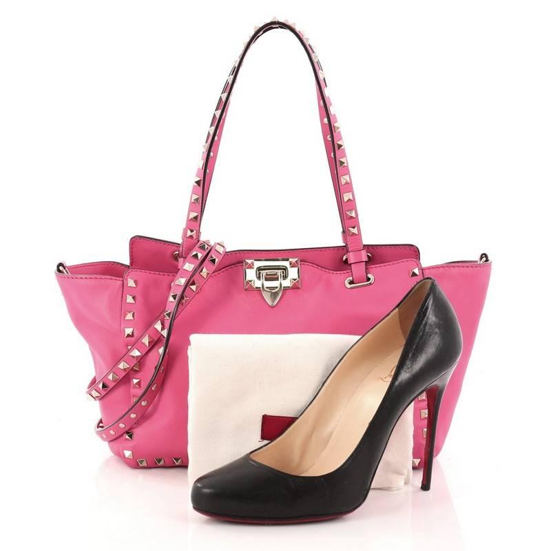 This authentic Valentino Rockstud Tote Soft Leather Small mixes edgy style with luxurious detailing. Crafted from pink soft leather, this stylish tote features dual tall flat handles, gold-tone pyramid stud trim details, a signature clasp fastening,