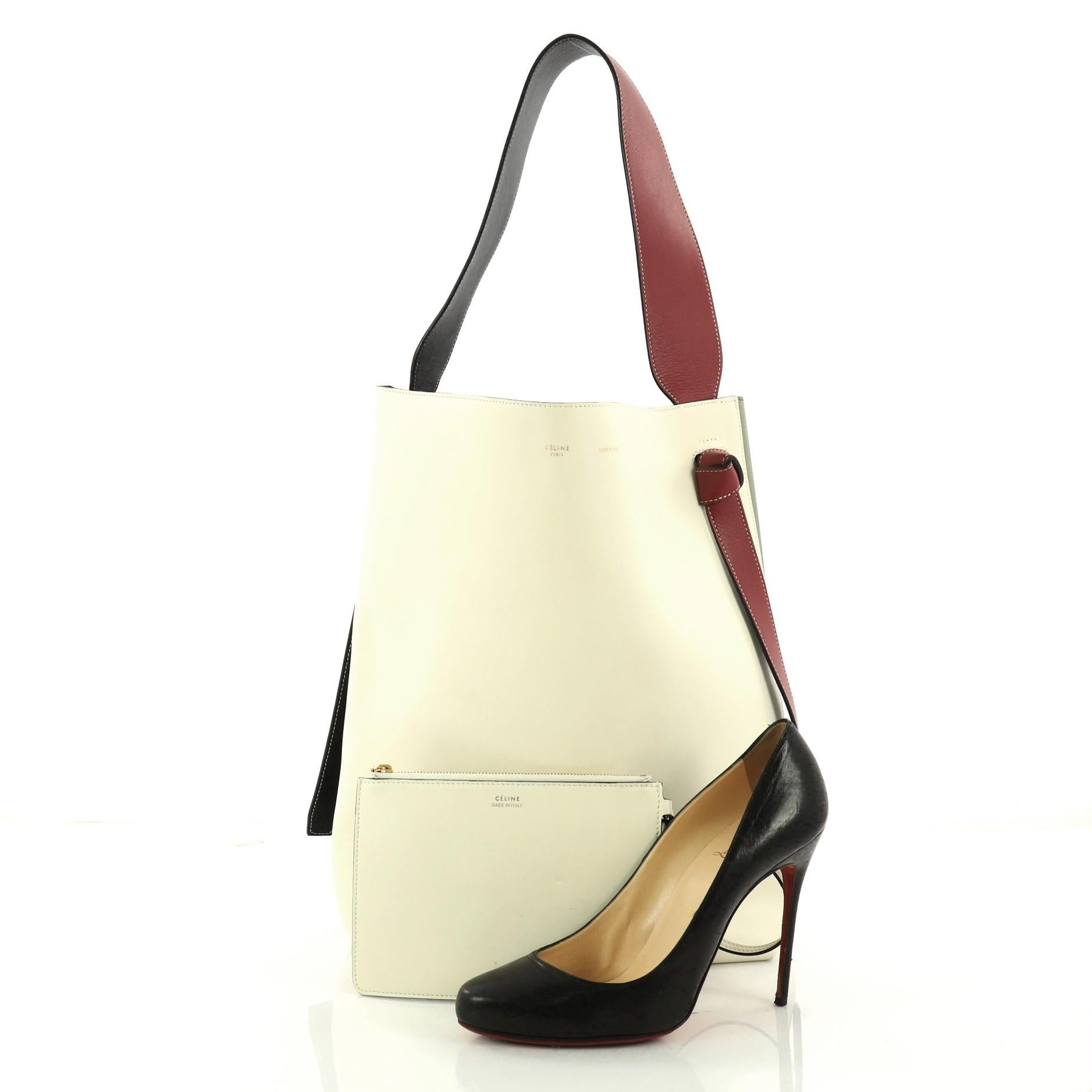 This authentic Celine Twisted Cabas Tote Calfskin Small is a youthful accessory made for everyday excursions. Crafted from off white, green, and red calfskin leather, this fresh tote features red and black leather looping shoulder strap with knot