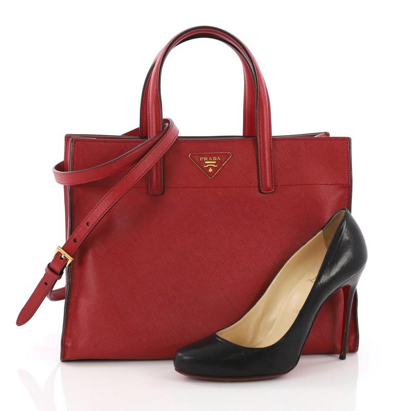 This Prada Soft Triple Pocket Convertible Tote Saffiano Leather, crafted from red saffiano leather, features dual-slim leather handles, two exterior compartments, and gold-tone hardware. Its wide open top showcases a black leather interior divided