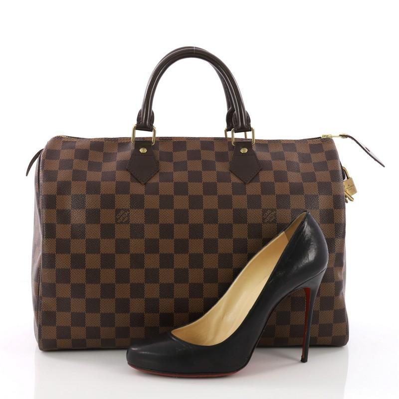 This Louis Vuitton Speedy Handbag Damier 35, crafted in damier ebene coated canvas, features dual rolled handles, dark brown leather trims and gold-tone hardware. Its top zip closure opens to a roomy red fabric interior with slip pocket.