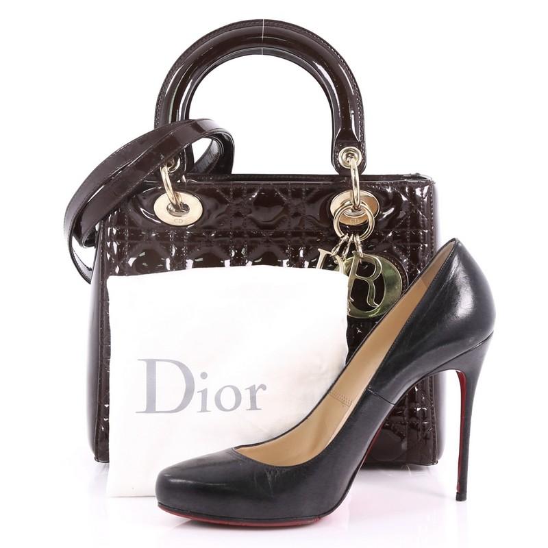 This Christian Dior Lady Dior Handbag Cannage Quilt Patent Medium, crafted in brown cannage quilt patent leather, features short dual handles with sleek Dior charms and gold-tone hardware. Its top zip closure opens to a brown fabric interior with a