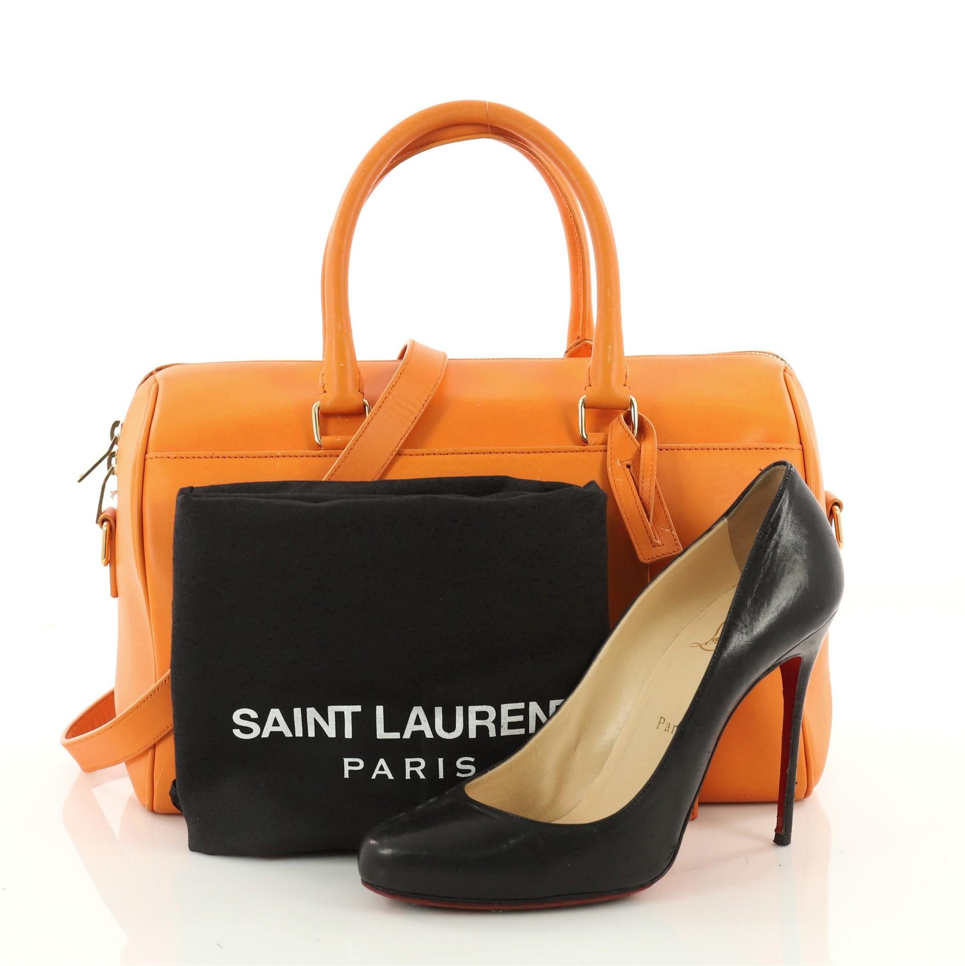 This authentic Saint Laurent Classic Duffle Bag Leather 12 is a sleek miniature bag. Crafted from orange leather, this petite duffle features dual-rolled handles, Saint Laurent logo in gold writing, protective base studs, and gold-tone hardware