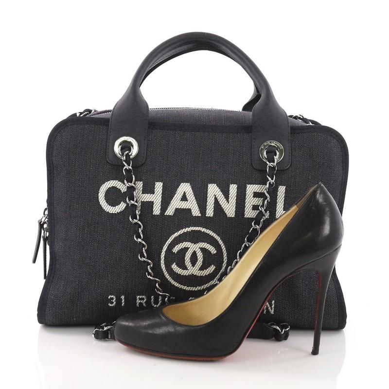 This Chanel Deauville Bowling Bag Denim Large, crafted in blue denim, features dual leather handles, woven in leather chain link strap with leather pads, and silver-tone hardware. Its zip closure opens to a blue fabric interior with zip and slip