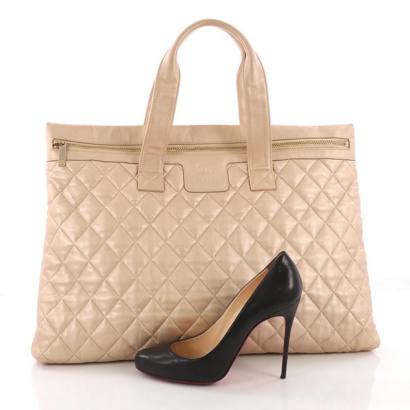 This Chanel Coco Cocoon Flat Tote Quilted Calfskin Large, crafted from beige metallic quilted calfskin, features dual flat leather handles and gold-tone hardware. Its zip closure opens to a burgundy leather interior zip pocket. Hologram sticker