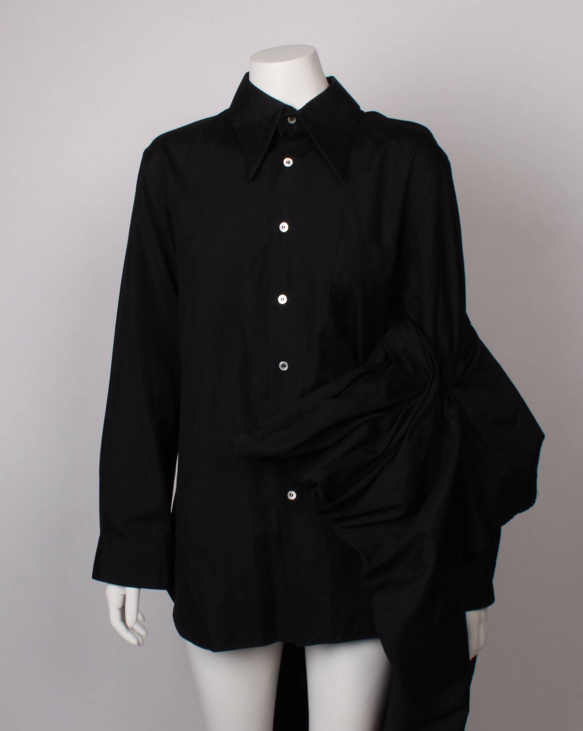 Comme Des Garcons

Peaked collar. Slit in one shoulder. Convertible bustle/wrap/cape that attaches at back of collar. Pearlescent charcoal shirt buttons. One patch breast pocket. 

100% cotton 
Dated: 2003AD

Length of shirt - 75cm
Total length of