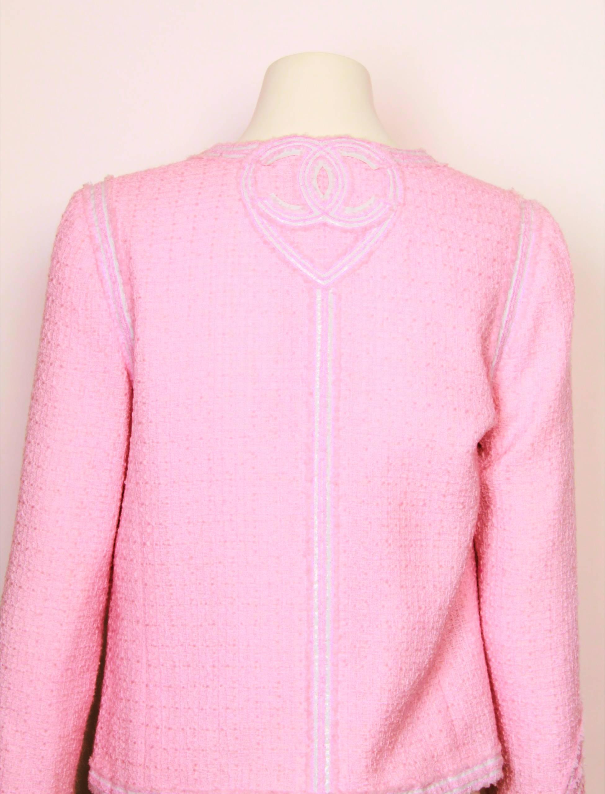 CHANEL Tweed Jacket in soft pink with white vinyl Chanel logo and heart  decorative feature on back neck and sleeve hem.
Entire jacket is edged in white vinyl strips. Jacket is fully lined in silk custom Chanel embossed lining with chain detailed