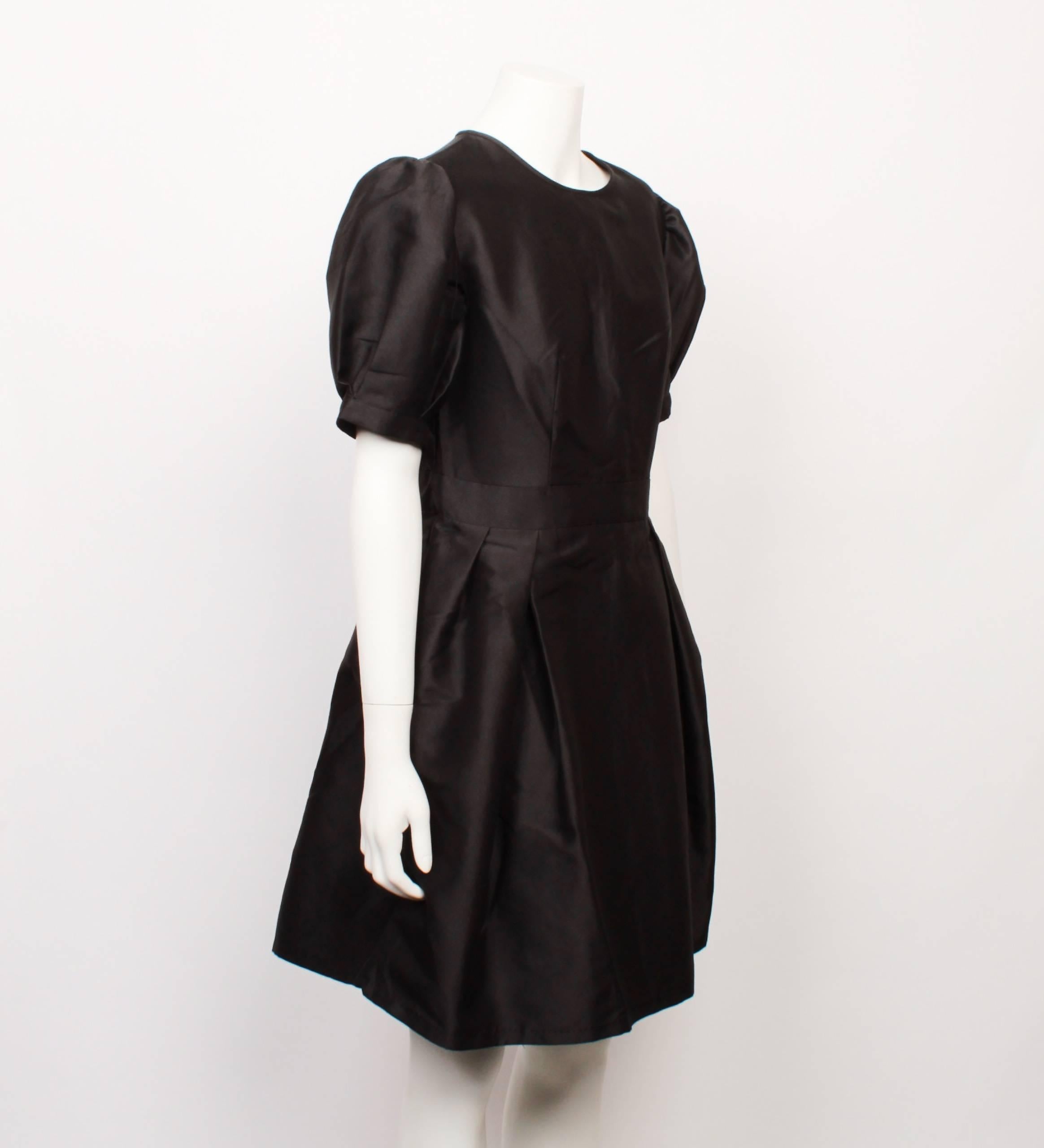 Cute and classic Christian Dior black silk satin party dress features a fitted shell bodice with high round neckline and gathered puffed sleeves. Skirt is knee length and has knife pleats at the waist to create a lovely quintessential Dior full