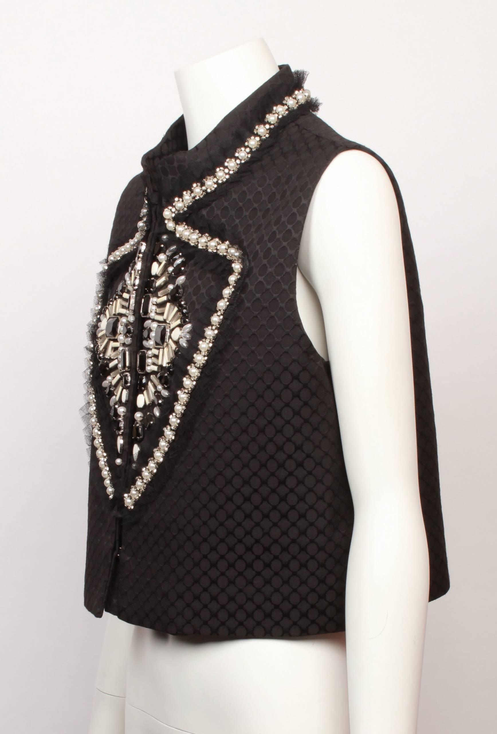 Givenchy  black cropped vest with jewelled front embellishment. 
Jewels are in tones of black, white, silver and pearl and continue across the back neckline .
Base fabric is black textured faille. 
Fully lined with hook and eye front closure. 