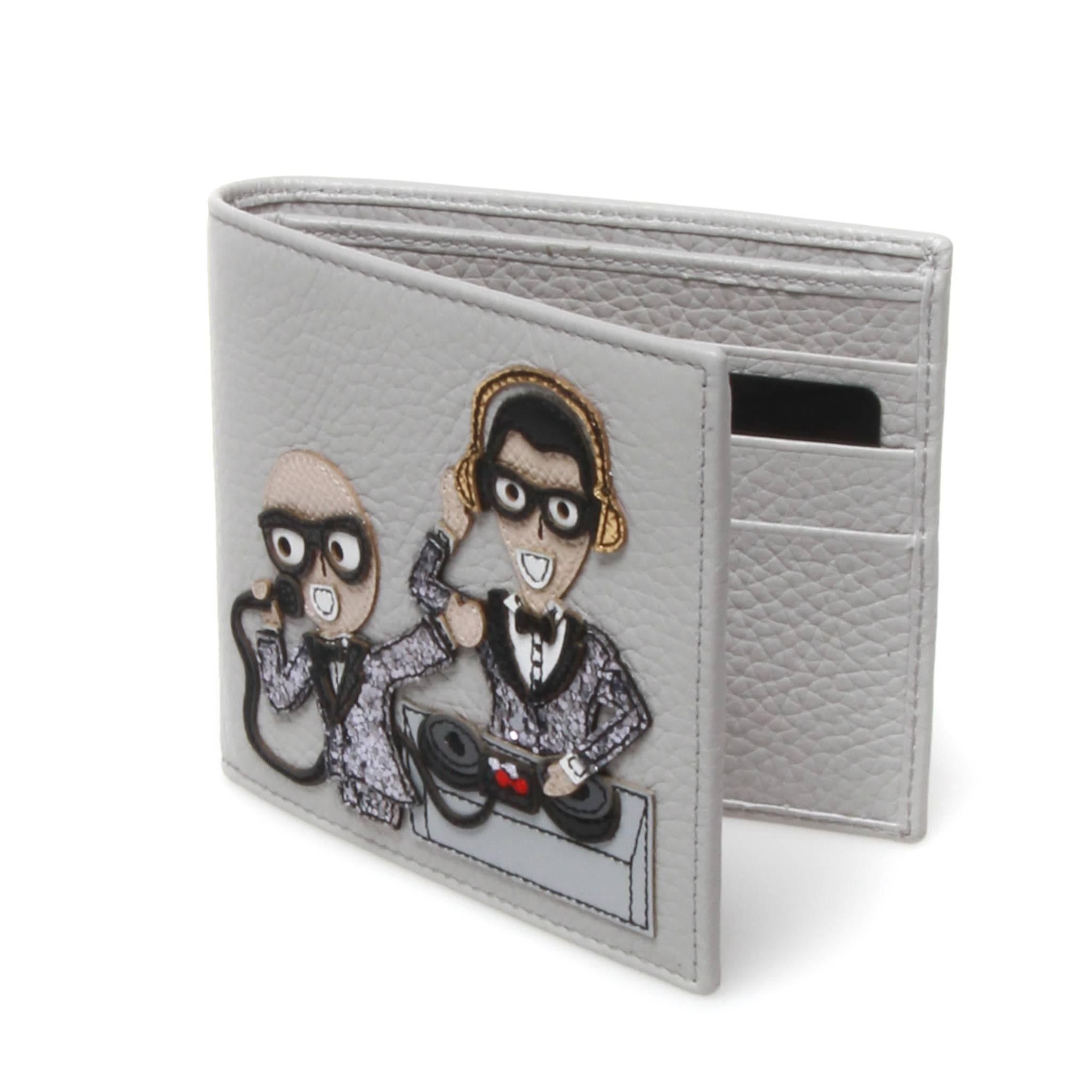 Dolce and Gabbana white bi-fold dauphine calf leather wallet featuring a playful DJ themed patch applique graphic. Interior features 6 card slots and sleeve for notes and receipts. Gold brand name stamp to back side. 