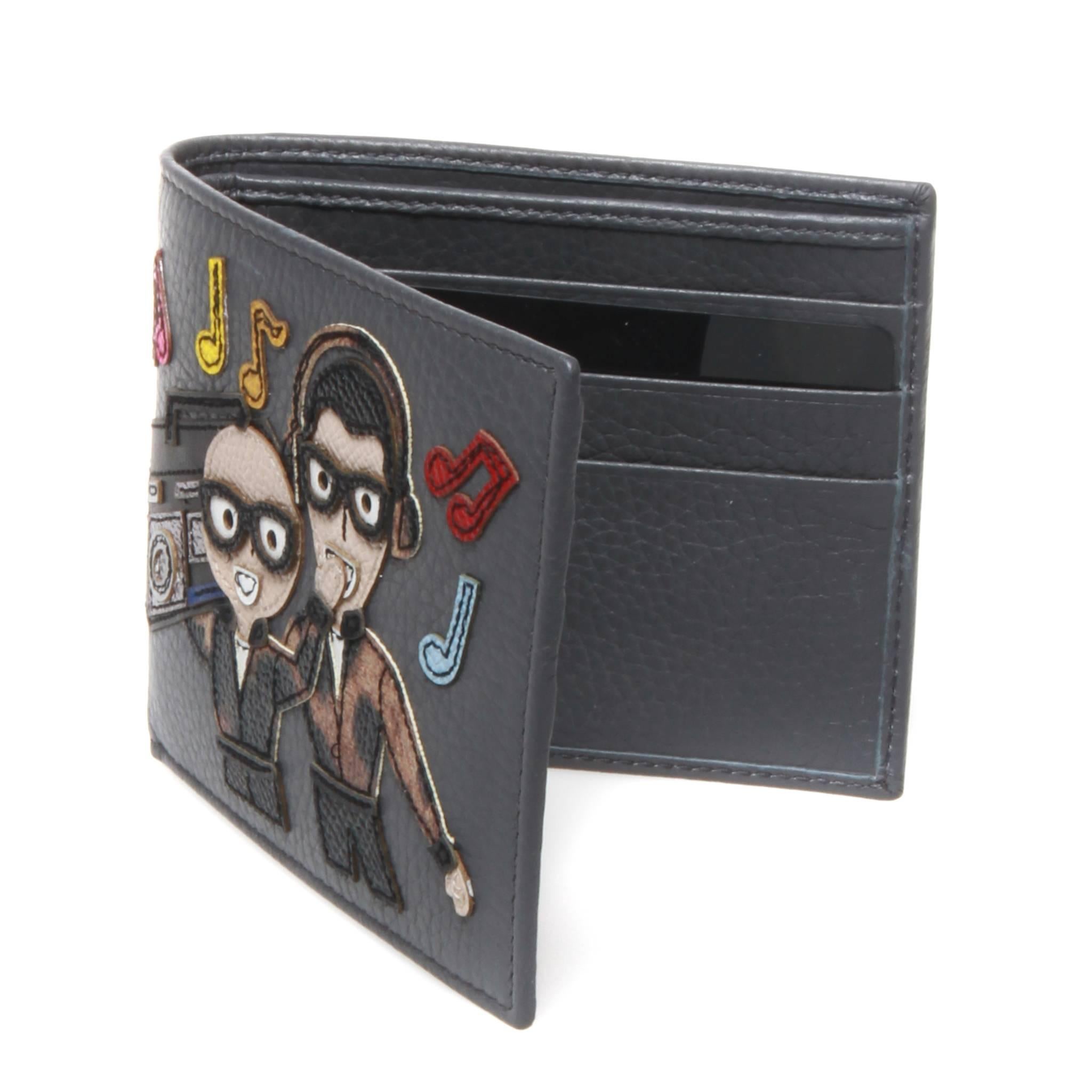 Dolce and Gabbana dark grey bi-fold dauphine calf leather wallet featuring a music themed patch graphic. Interior features 6 card slots and sleeve for notes and receipts. Gold printed brand name at back side.