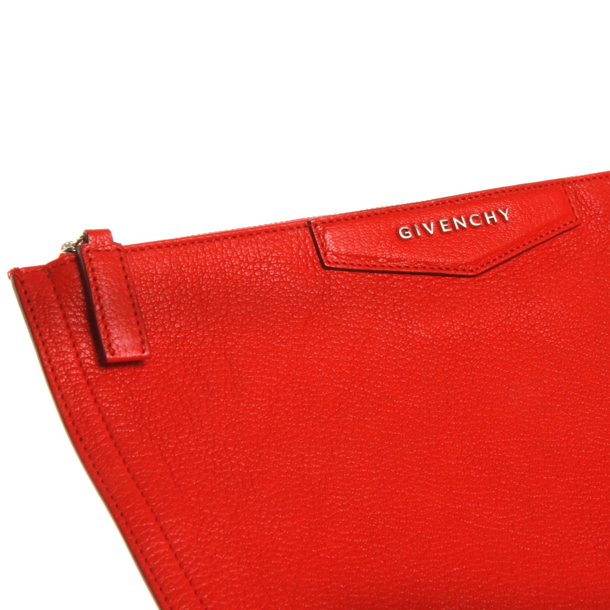 Scarlet red grained leather Givenchy Antigona pouch with silver-tone hardware, logo accent at front, beige woven canvas lining and zip closure at top. Includes dust bag. 