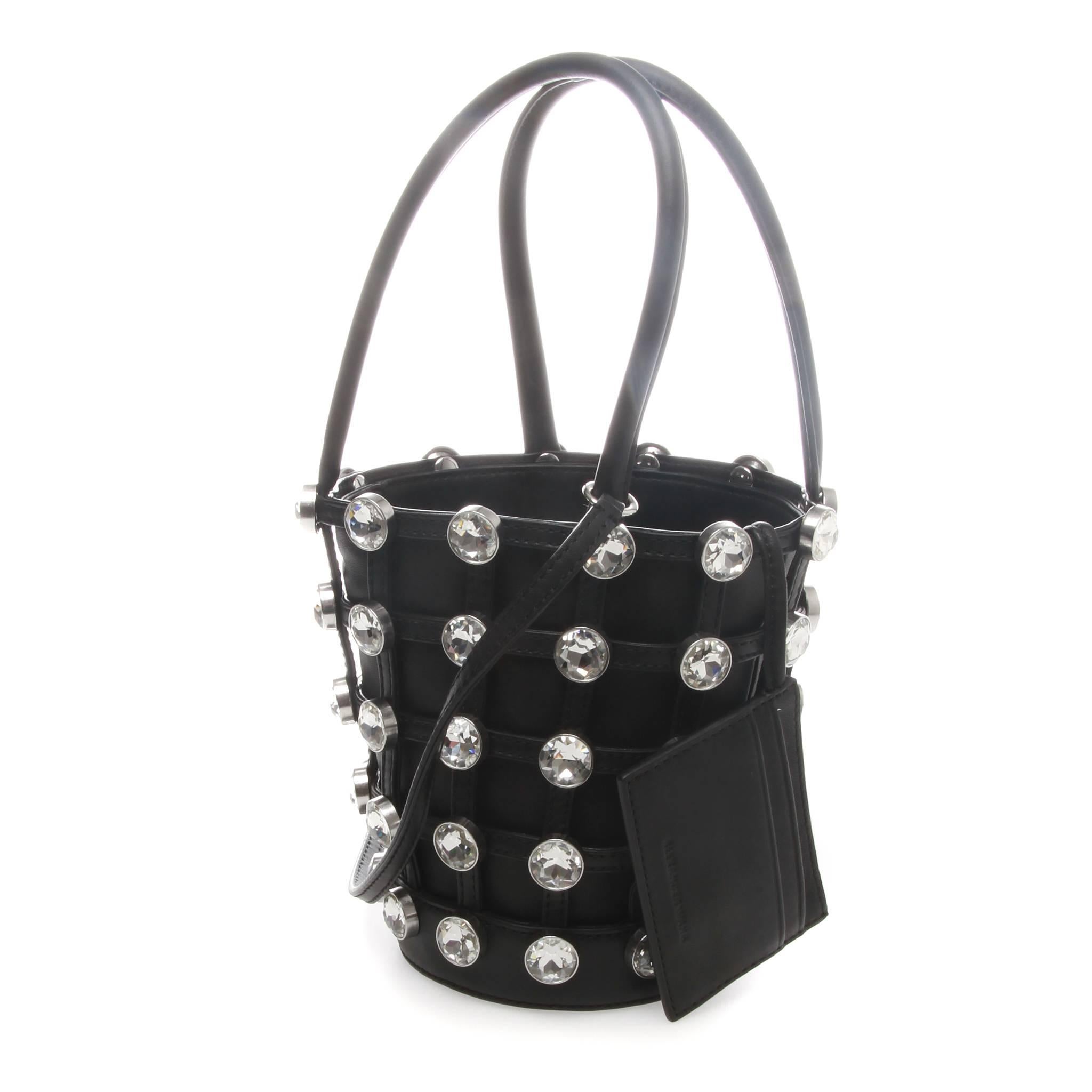 Alexander Wang mini Roxy top handle bucket bag in black nappa leather. Cage-style overlay featuring crystal-cut detailing throughout. Twin rolled carry handles. Lanyard with hoop hardware at handle base. Leather card holder on lanyard at interior.