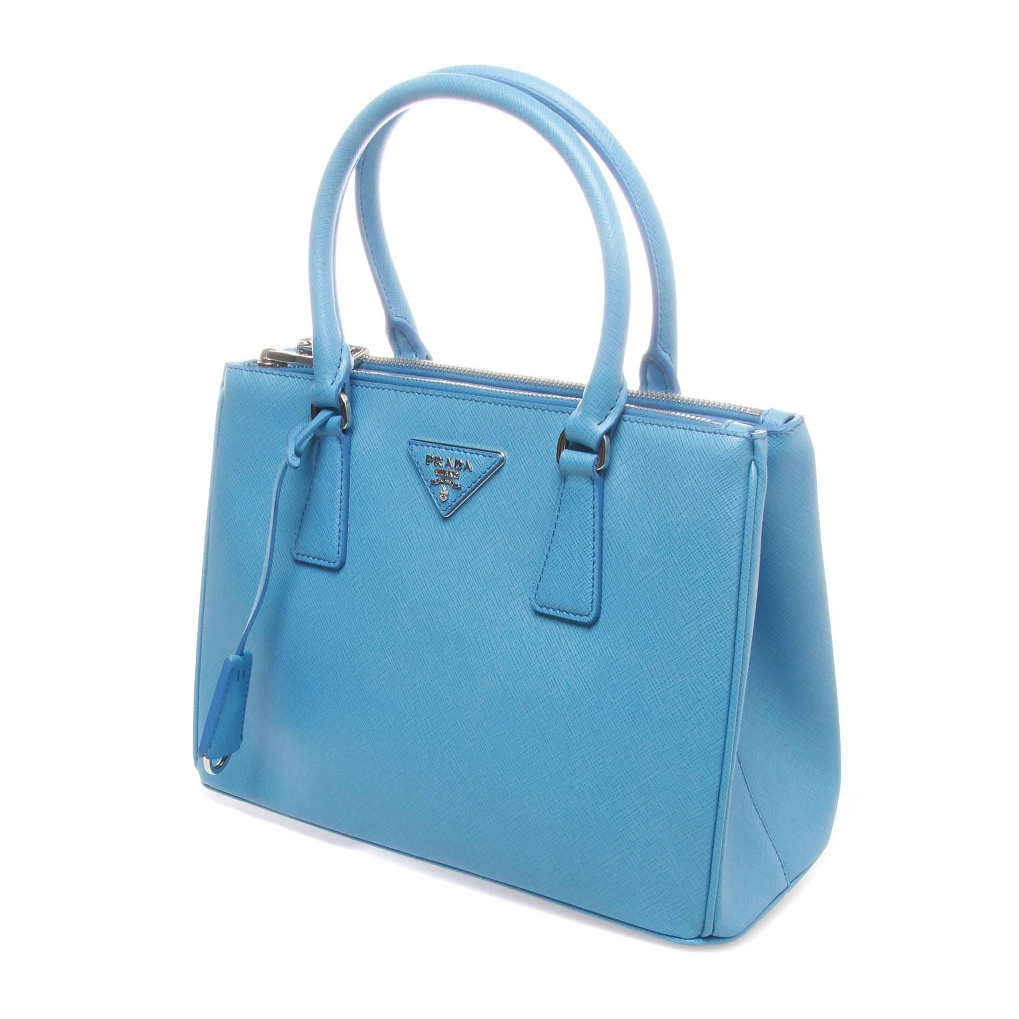 28cm Prada Galleria shopping bag in sea blue saffiano lux leather. Featuring silver-tone hardware, dual rolled top handles, single adjustable shoulder strap, logo placard at front face, dual snap expansions at sides, protective feet at base, tonal