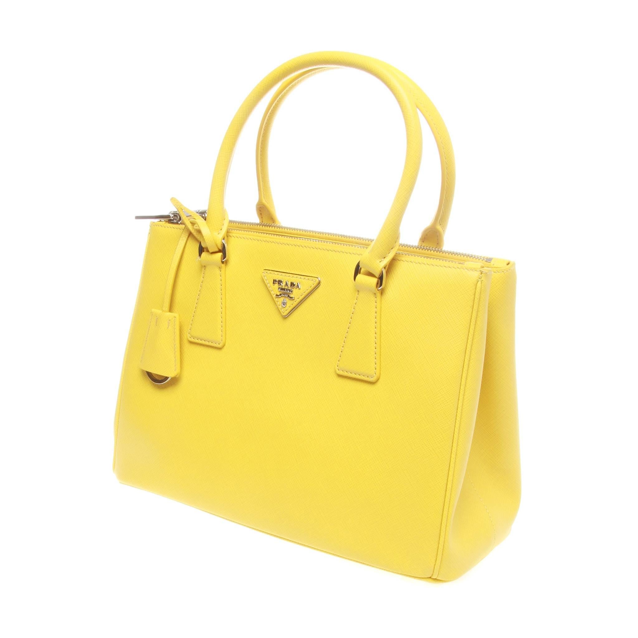 28cm Prada Galleria shopping bag in yellow saffiano lux leather. Featuring silver-tone hardware, dual rolled top handles, single adjustable shoulder strap, logo placard at front face, dual snap expansions at sides, protective feet at base, tonal