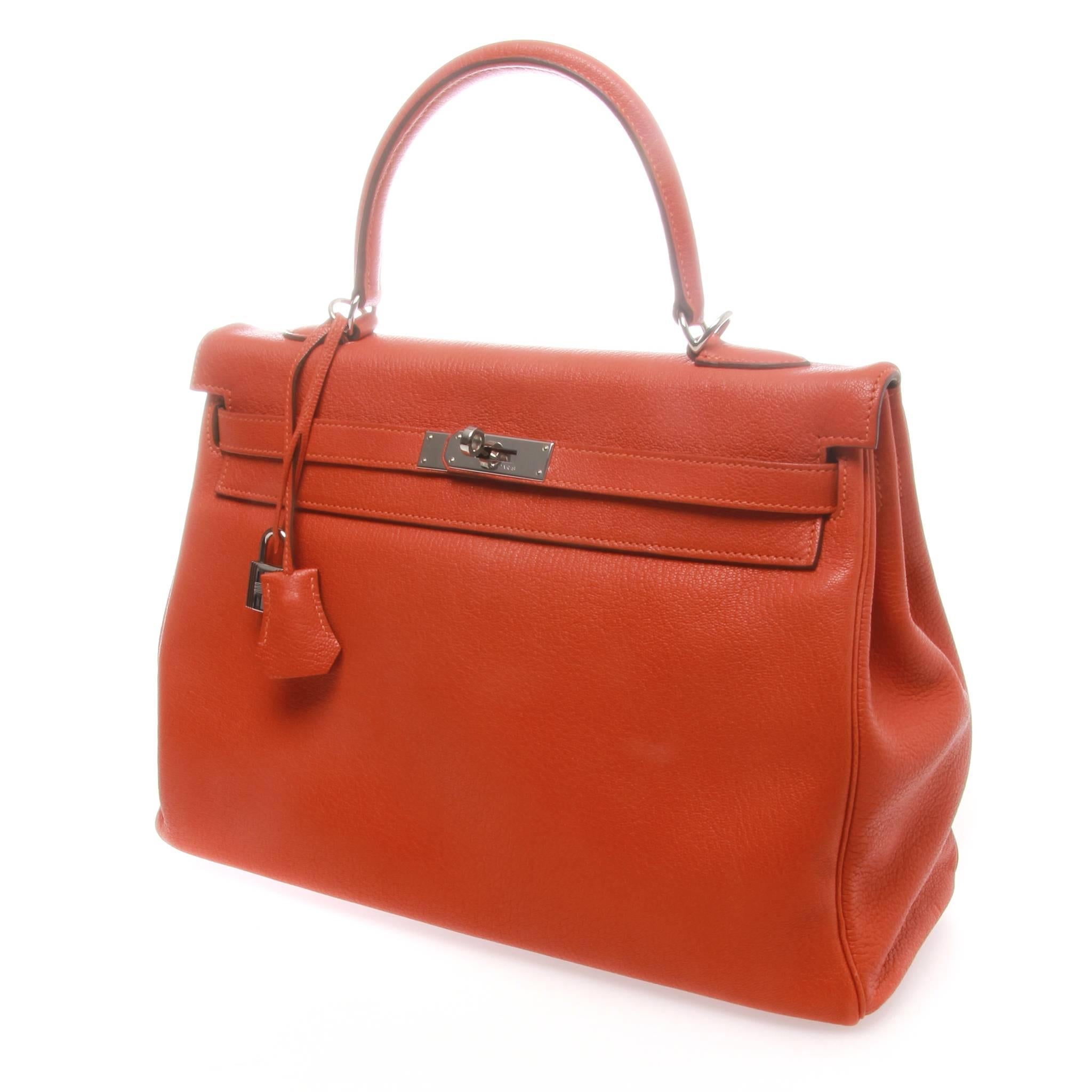 Orange Chevre Mysore leather Hermès Kelly Retourne 35 with palladium hardware, optional shoulder strap, single flat top handle, tonal leather interior, three pockets at interior walls; one with zip closure and flap with turn-lock closure at front.
