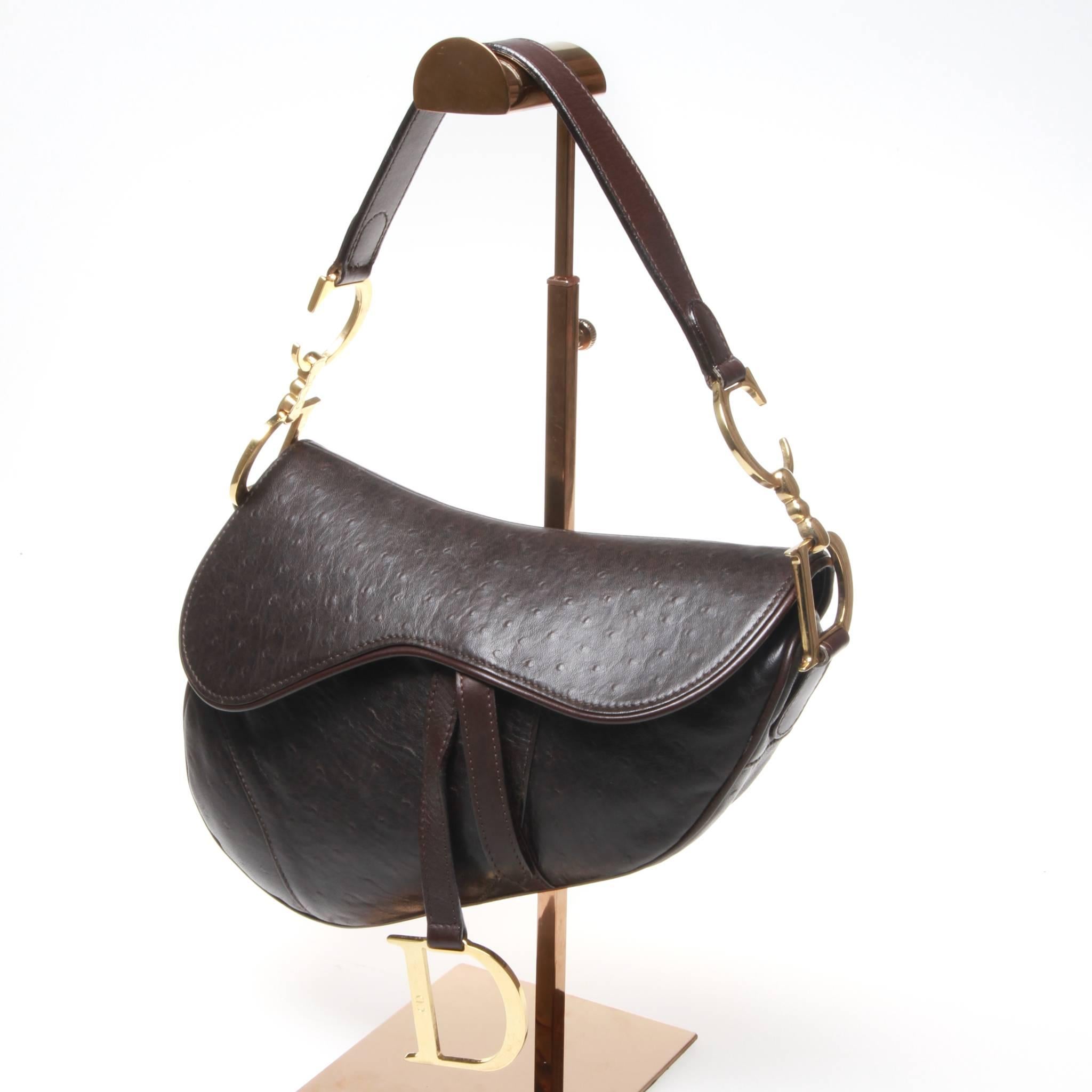 Dark chocolate brown ostrich leather Christian Dior Saddle bag with brushed gold tone hardware, single flat shoulder strap with logo accents, single exterior pocket, chocolate suede lining, single interior zip pocket and velcro closure at front