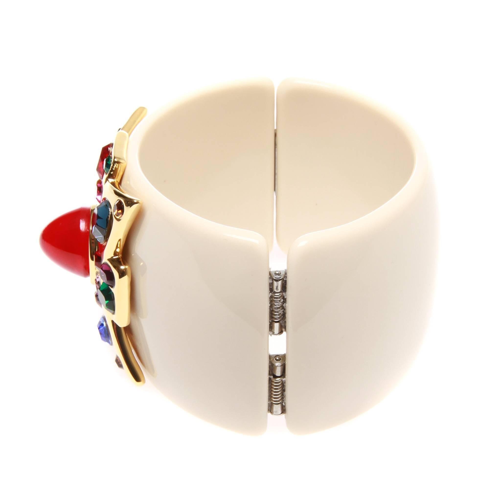 Kenneth Jay Lane cuff in white resin featuring a gold-tone Maltese cross embellished with multi-coloured glass stones. Magnetic closure.
