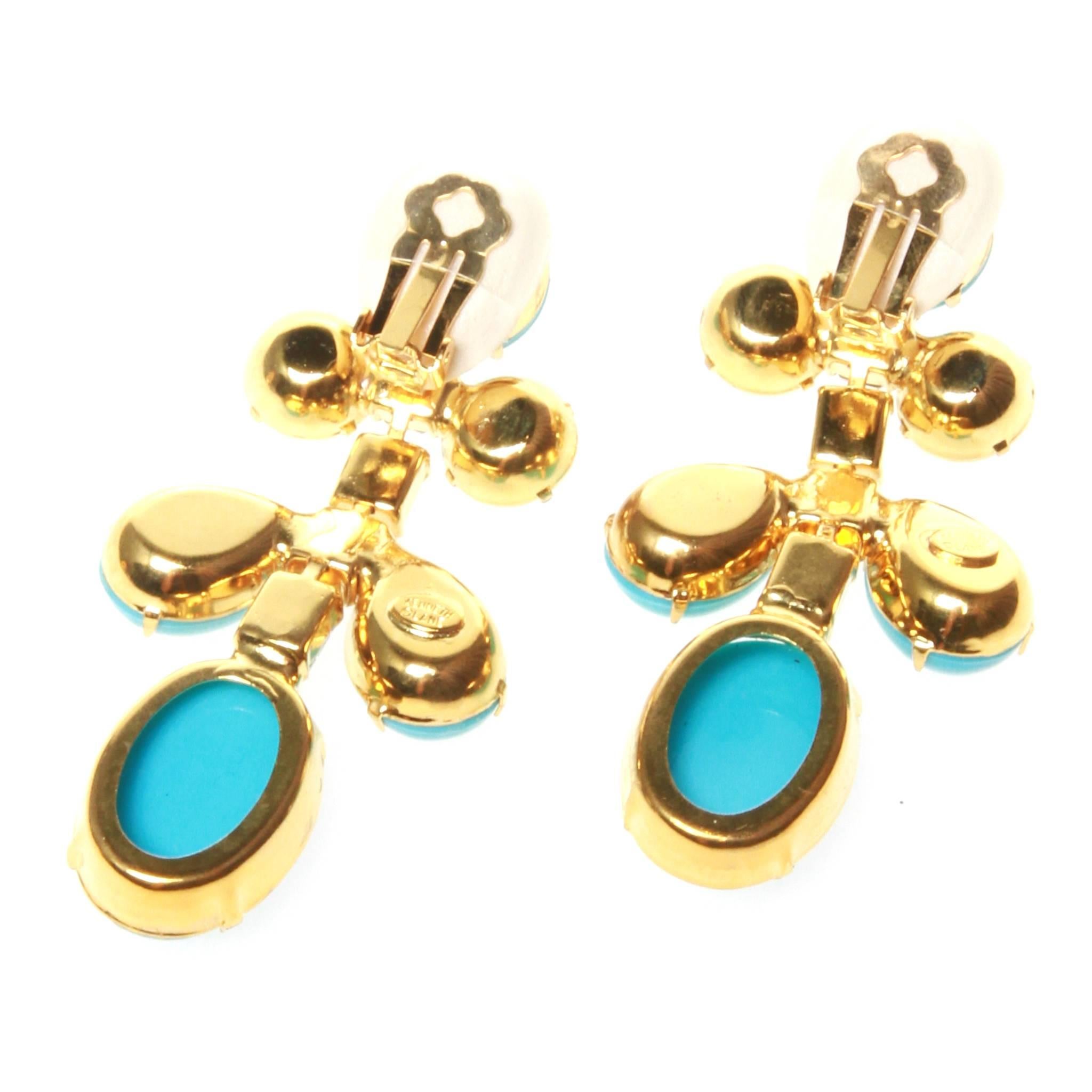 Kenneth Jay Lane clip on earrings in a gold-tone setting featuring blue stone off a clear crystal central strand. Brand stamp at back.