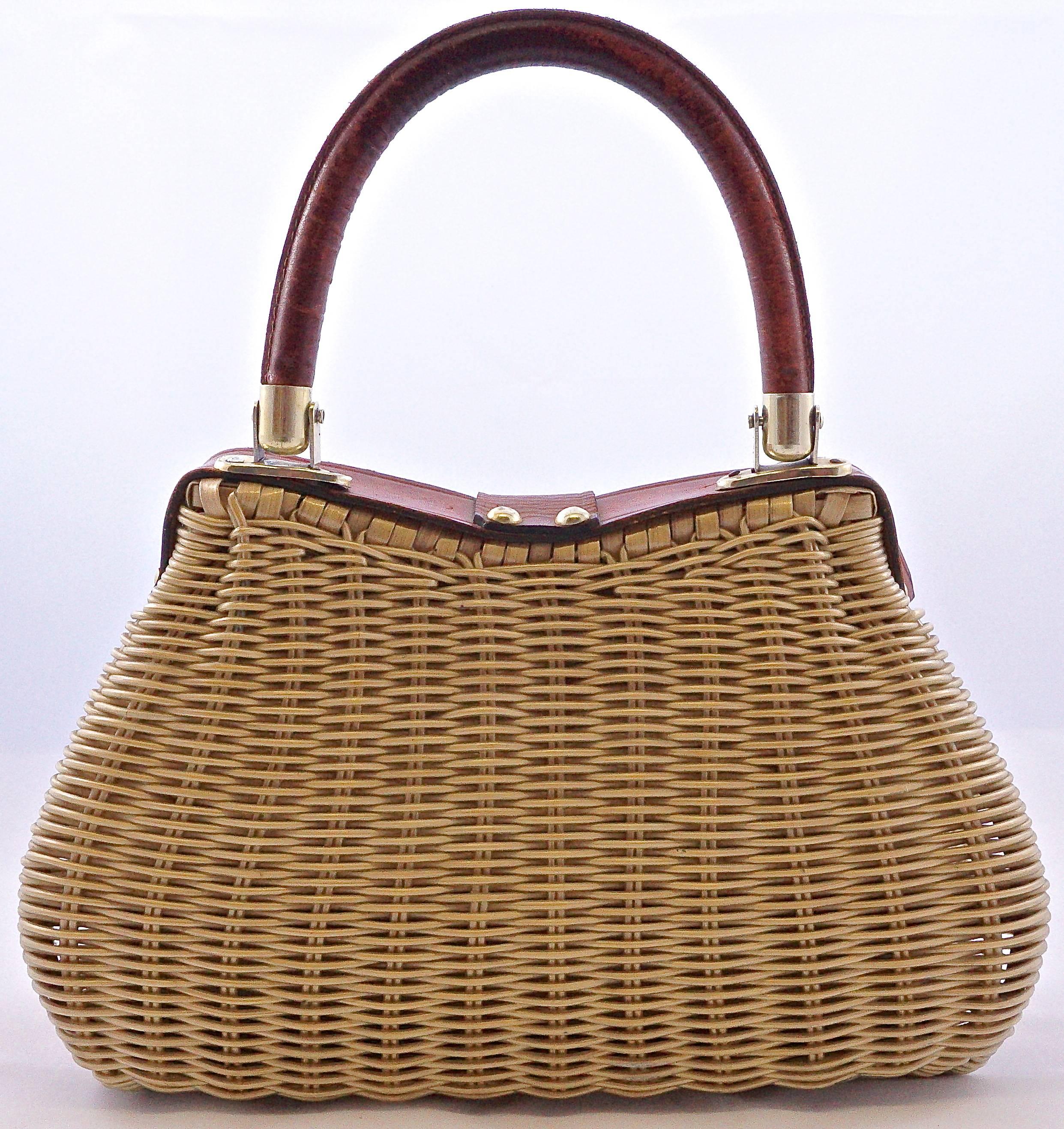 This stylish wicker bag, with dark tan leather detail and gold tone metal fittings, was made in British Hong Kong, circa 1960s. Measuring maximum width 27.5cm, 10.8 inches, by maximum height 19cm, 7.5 inches. Handle drop 13.3cm, 5.2 inches. The