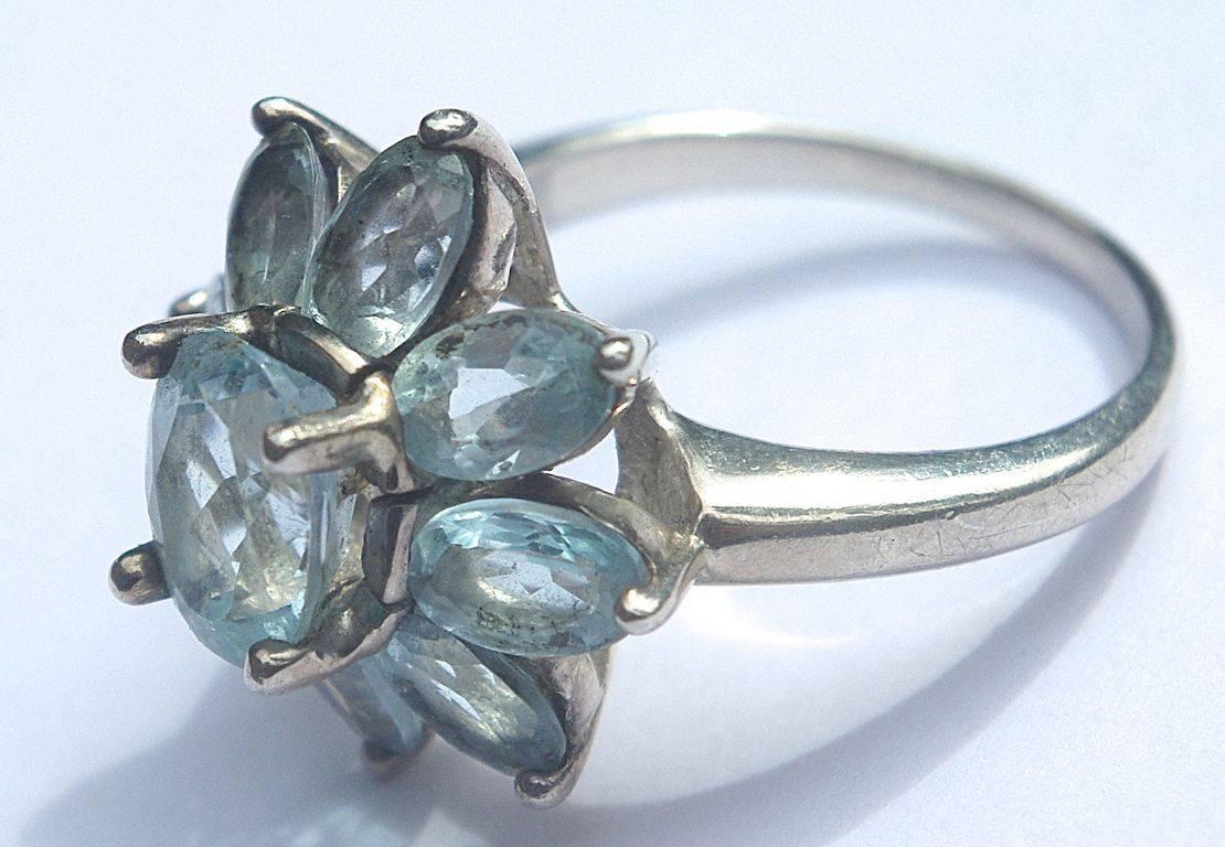 Silver ring featuring an oval faceted aqua blue glass stone, surrounded by eight smaller stones. Ring size UK O / US 7, and stamped 925. The front measures 1.8cm / .71 inches by 1.8cm / .71 inches, and the setting is depth 1cm / .39 inches.

This is