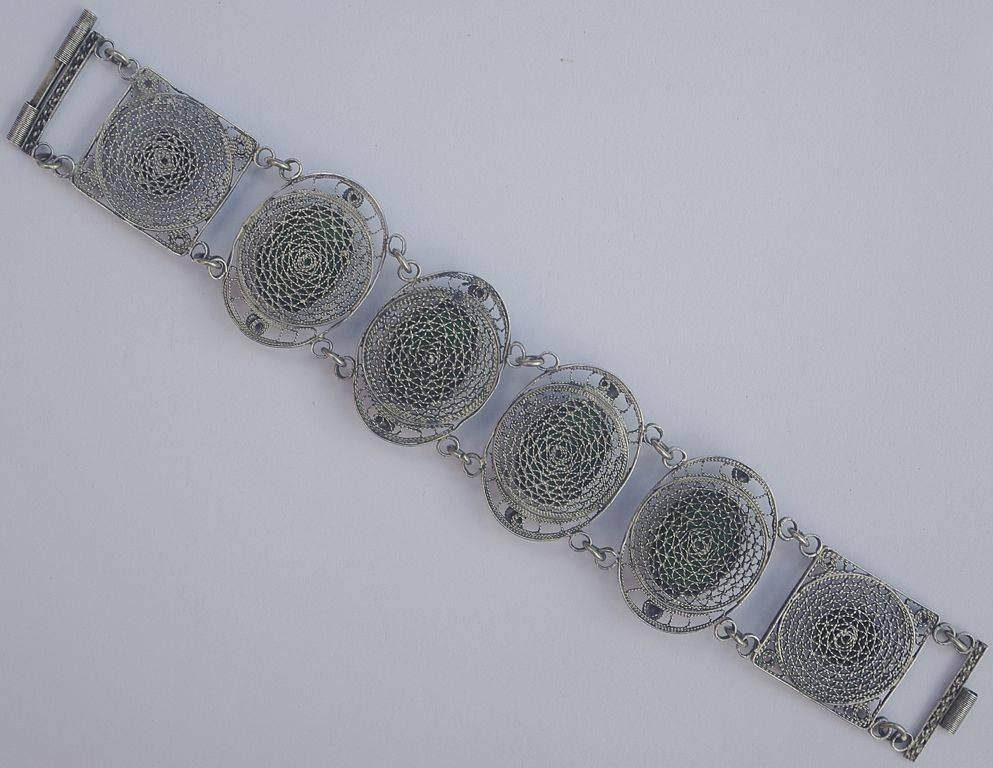 Chinese silver filigree bracelet featuring four faux green jade glass cabochons set in an intricate scallop edge bezel. It has double link connectors, and is circa 1930s. The two end links have round shiny silver circles with a rope twist edging.