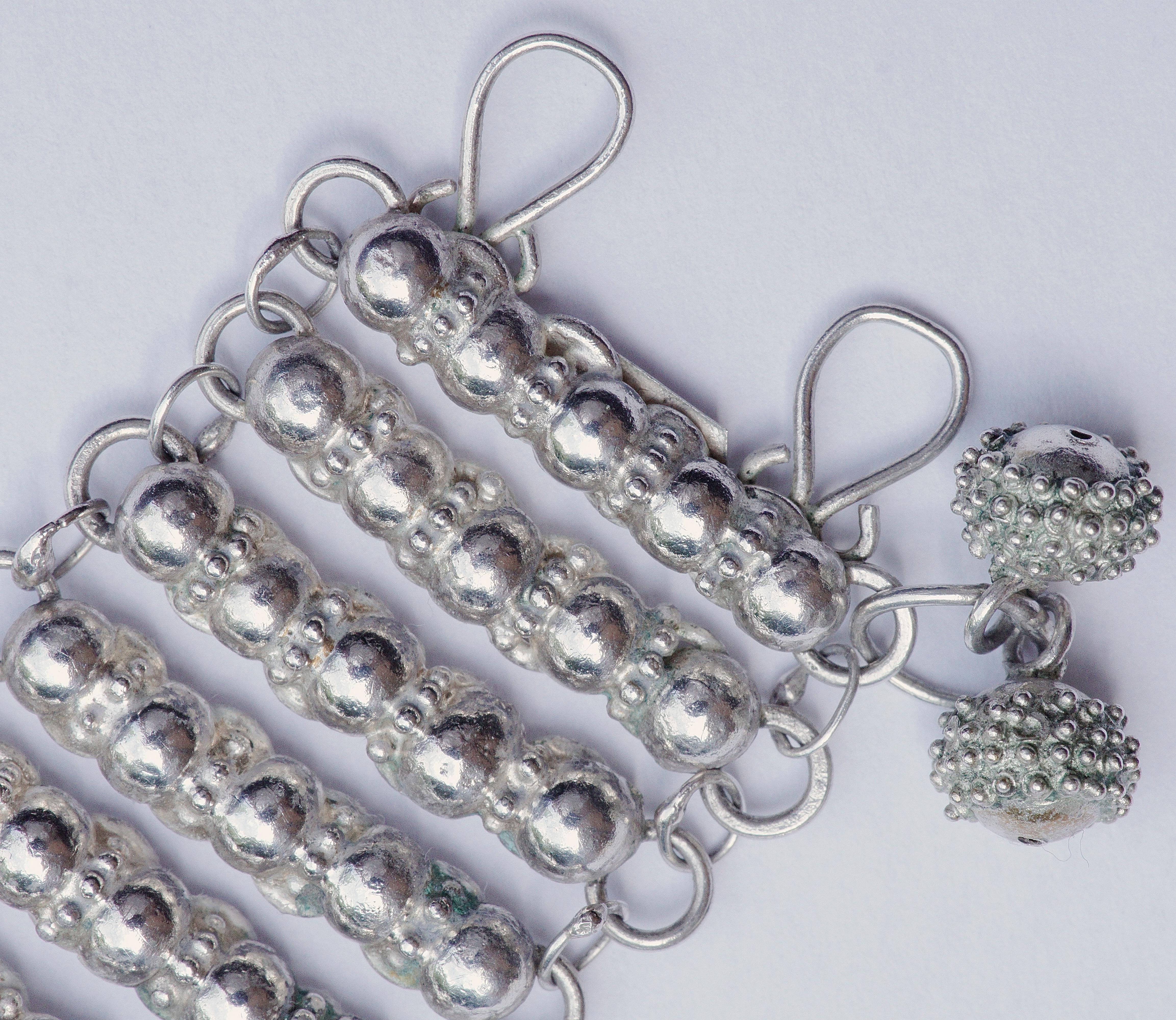 Bracciale in argento fatto a mano di qualità insolita, con maglie dal design a sfera e due ciondoli decorativi. Ha il timbro Silver Nigeria ed è testato per l'argento.

Misura 18,5 cm di lunghezza e 2,6 cm di larghezza. Il retro presenta qualche