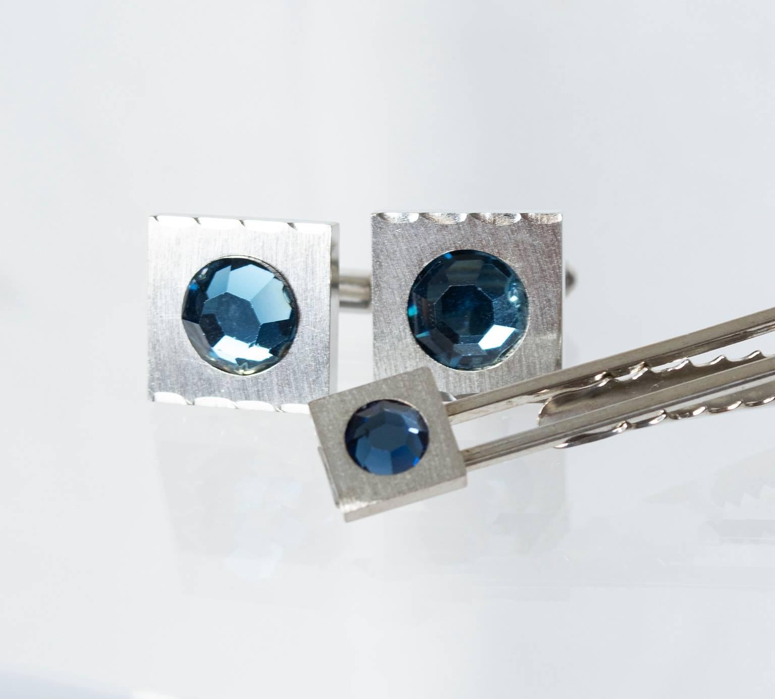 Substantial yet still understated, this tie bar and cuff link set speaks volumes at a whisper. Elegant brushed silver provides the perfect counterpoint to soothing aquamarine crystals; the fluted beveled edges are a bonus. 

Tie bar and cuff link