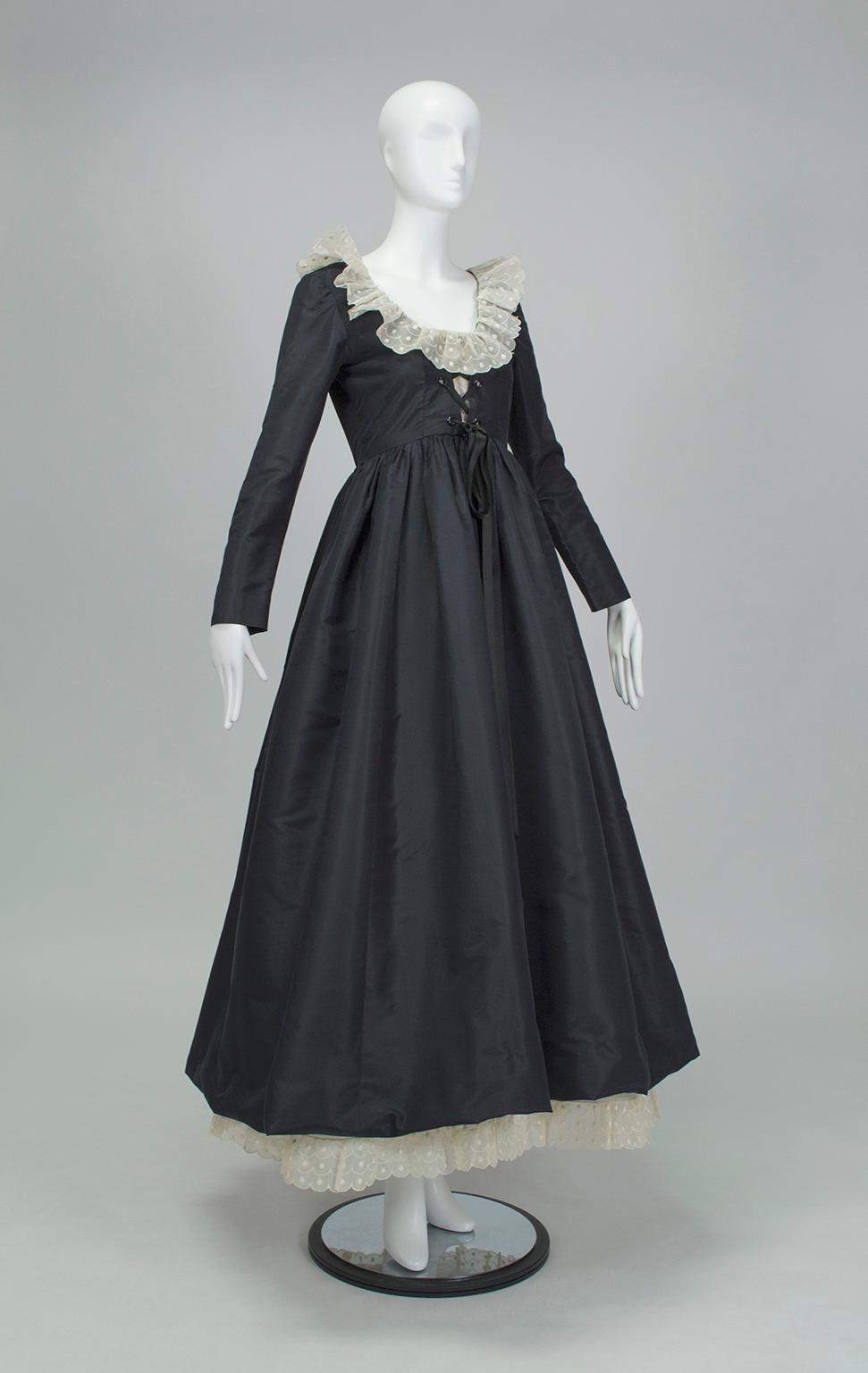 Navy blue Elizabethan style gown with long sleeves, close-fitting bodice and full skirt.  Bodice features low scooping neckline with 3” antique white scalloped organza eyelet ruffle and corset-laced front threaded with black satin ribbon; matching