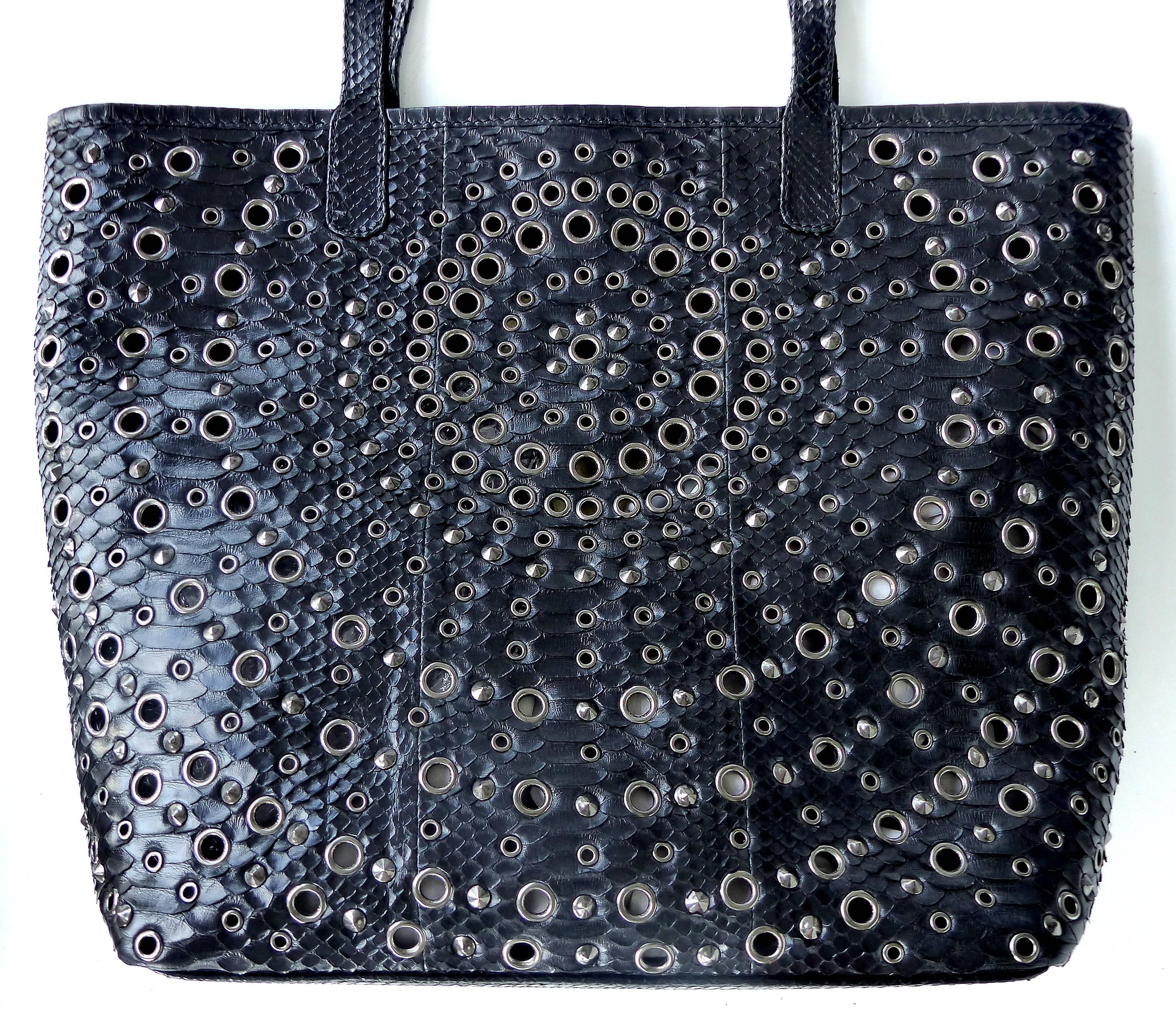
Offered for sale is a large perforated and studded rock python tote bag by Glen Arthur Designs for GaBag Co. This open tote has one zippered exterior pocket and magnetic tab closures. The perforated studs are stainless steel. The interior is lined